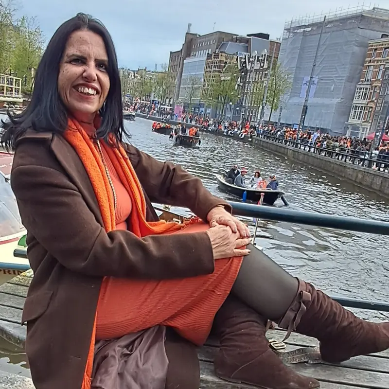 Lucyana sorrindo sentada à beira de um canal de Amsterdam.