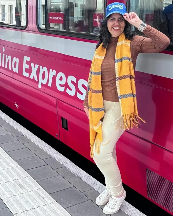 Lucyana Vega sorrindo ao lado do trem Bernina Express, na Suíça.