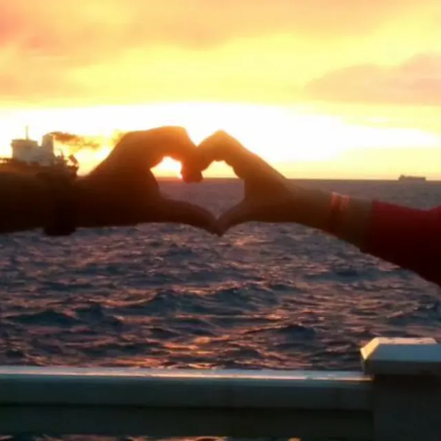 Mãos formando um coração contra o pôr do sol no Caribe.