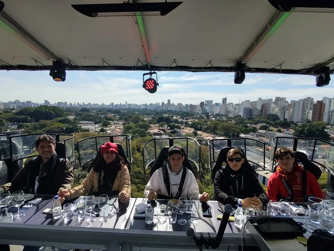 A família Vega reunida à mesa do Dinner in the Sky, suspensa no alto, com a cidade ao fundo.