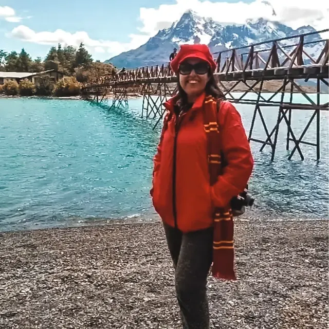 Viajante de casaco vermelho às margens de um lago turquesa em Torres del Paine, com montanhas nevadas ao fundo.