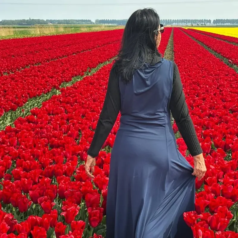 Lucyana caminhando entre fileiras de tulipas vermelhas.
