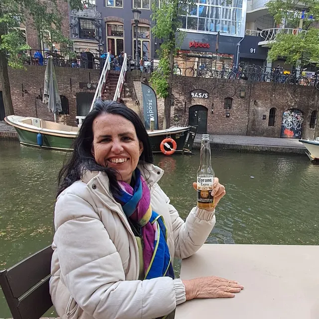 Viajante sorrindo com uma bebida à beira do canal Oudegracht.