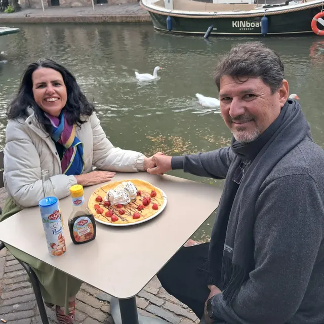 O casal tomando café com panqueca numa mesa à beira do canal em Utrecht.